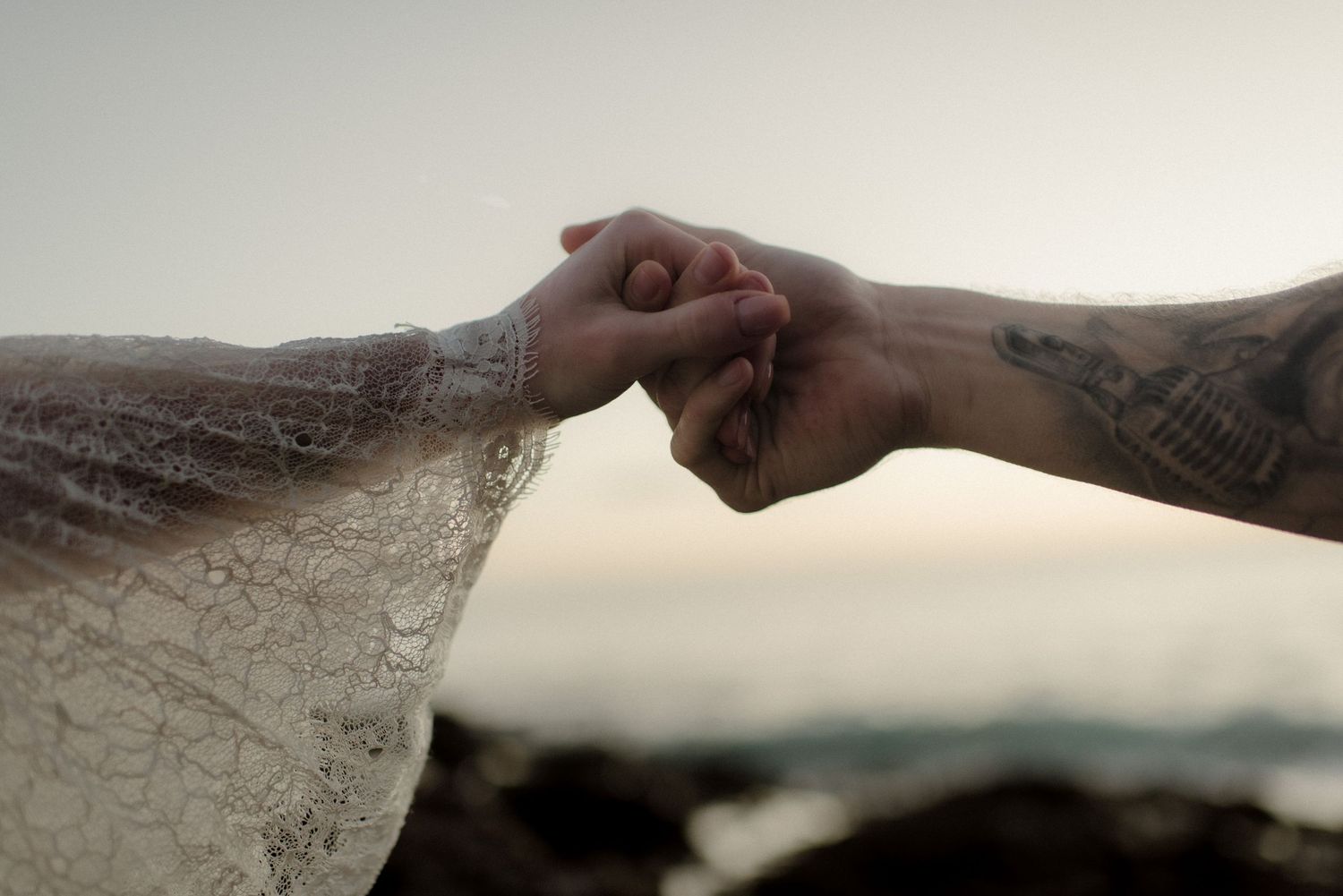 Two hands reach across a sandy beach at sunset to connect in a touching moment.