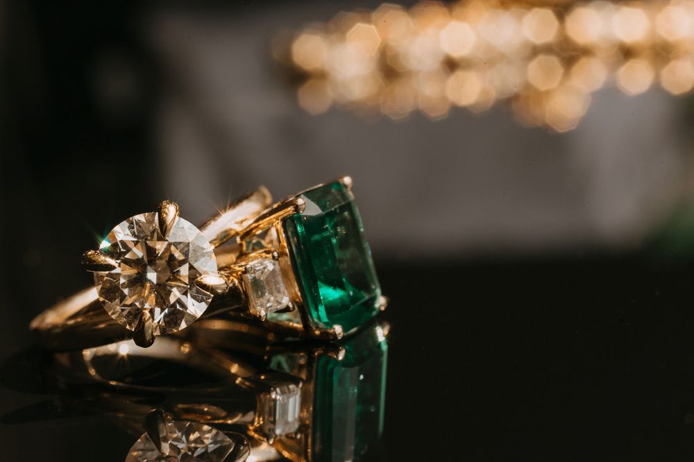 Close-up of two gold rings, one with a sparkling diamond and one with a vivid emerald gemstone.