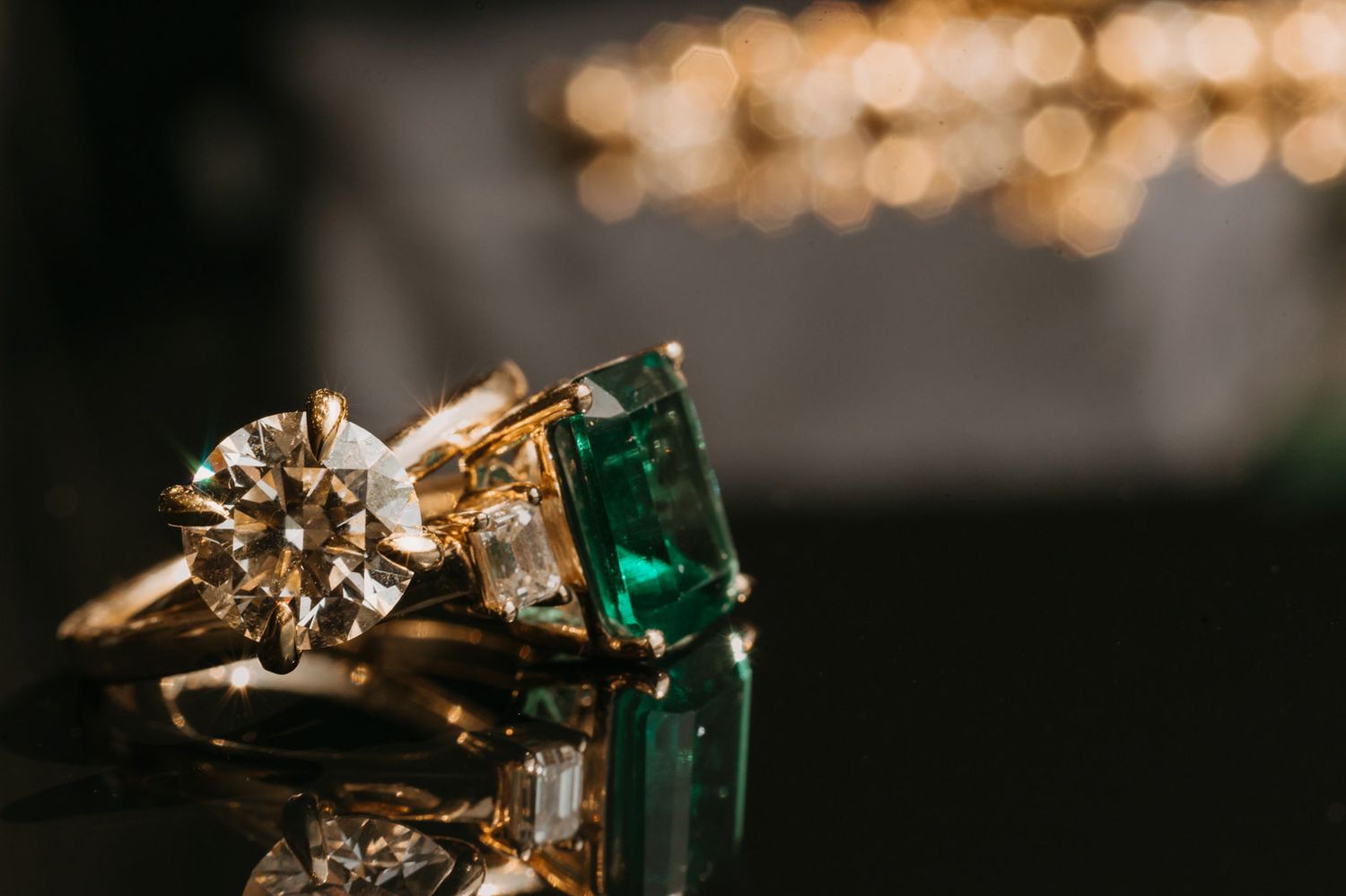 Close-up of two gold rings, one with a sparkling diamond and one with a vivid emerald gemstone.