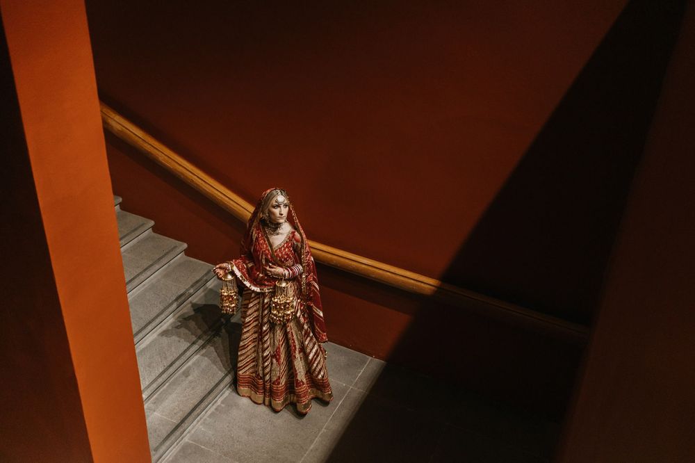 Indian bride in red and gold lehenga descending stairs in elegant bridal attire.