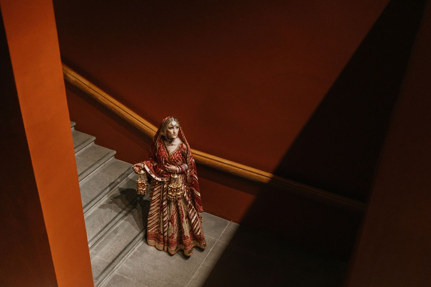 Indian bride in red and gold lehenga descending stairs in elegant bridal attire.