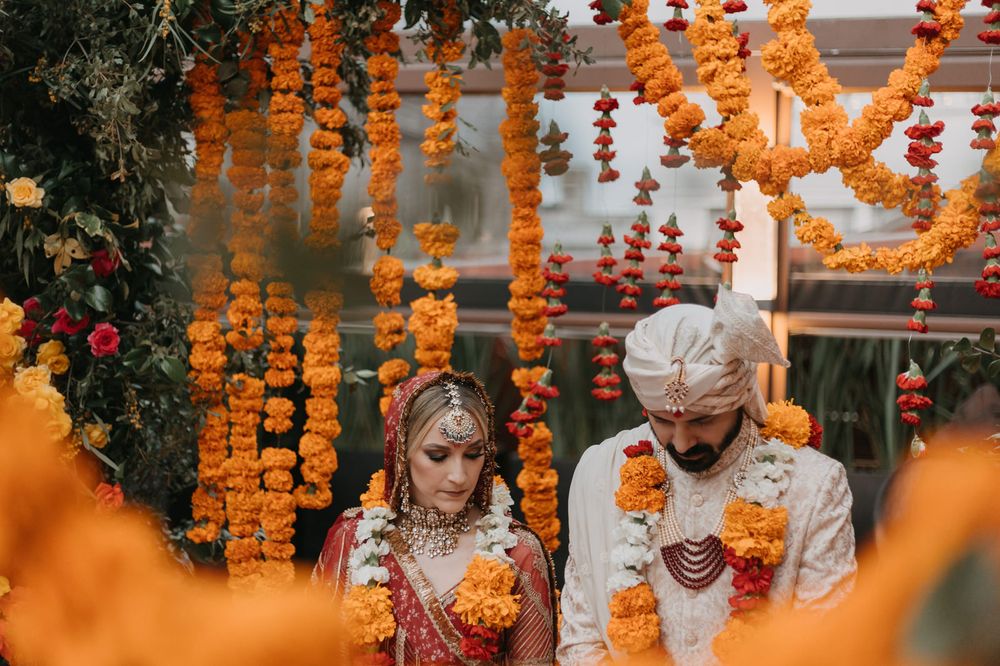 Indian bride and groom exchange garlands under vibrant marigold floral decorations during traditional Hindu wedding ceremony.
