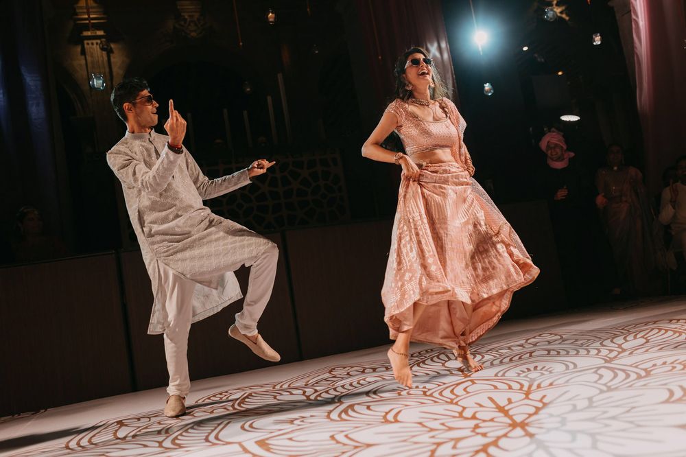Two dancers perform a vibrant Bollywood dance routine on a white dance floor at an elegant event.