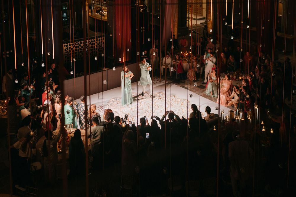 Aerial view of wedding reception with guests surrounding illuminated dance floor in grand venue.