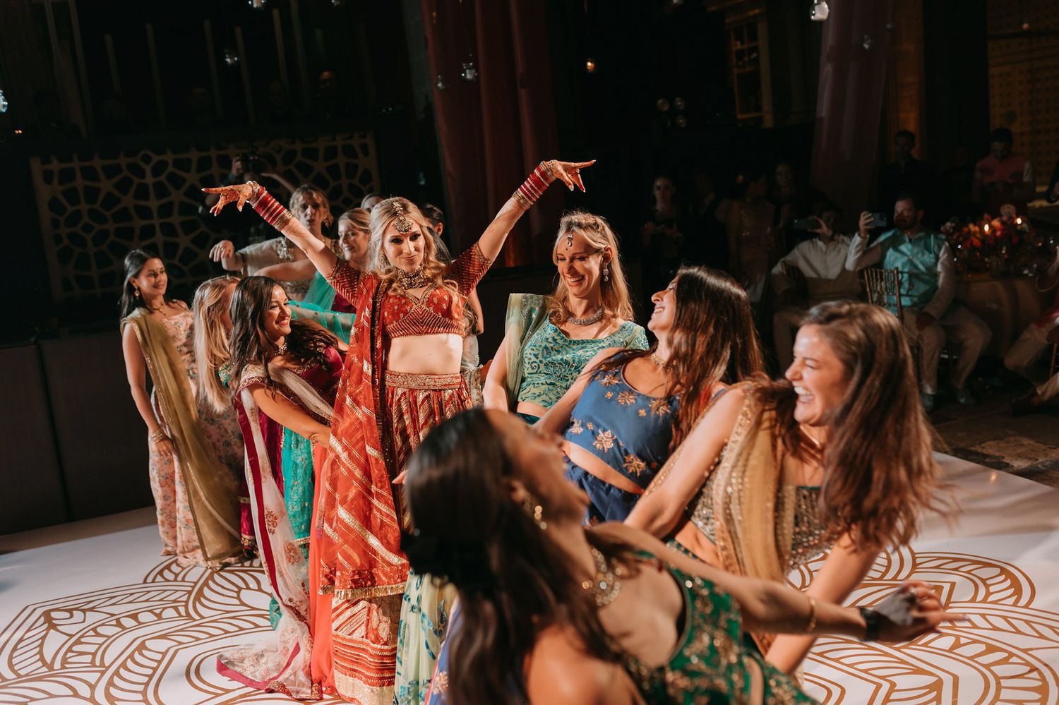 Women dancing together in colorful traditional attire at a festive Indian wedding celebration.