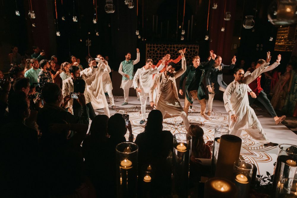 Performers in white costumes dancing on a decorated floor surrounded by candles and audience at an indoor event.