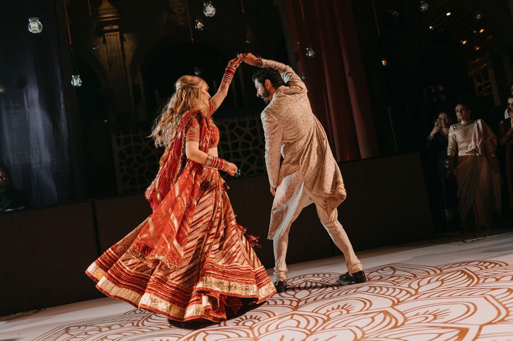 Couple performs a traditional Indian dance in matching red and gold wedding attire.