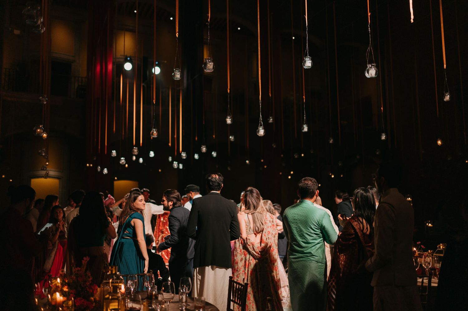 Guests mingle under hanging Edison bulb lights at an elegant indoor wedding reception.