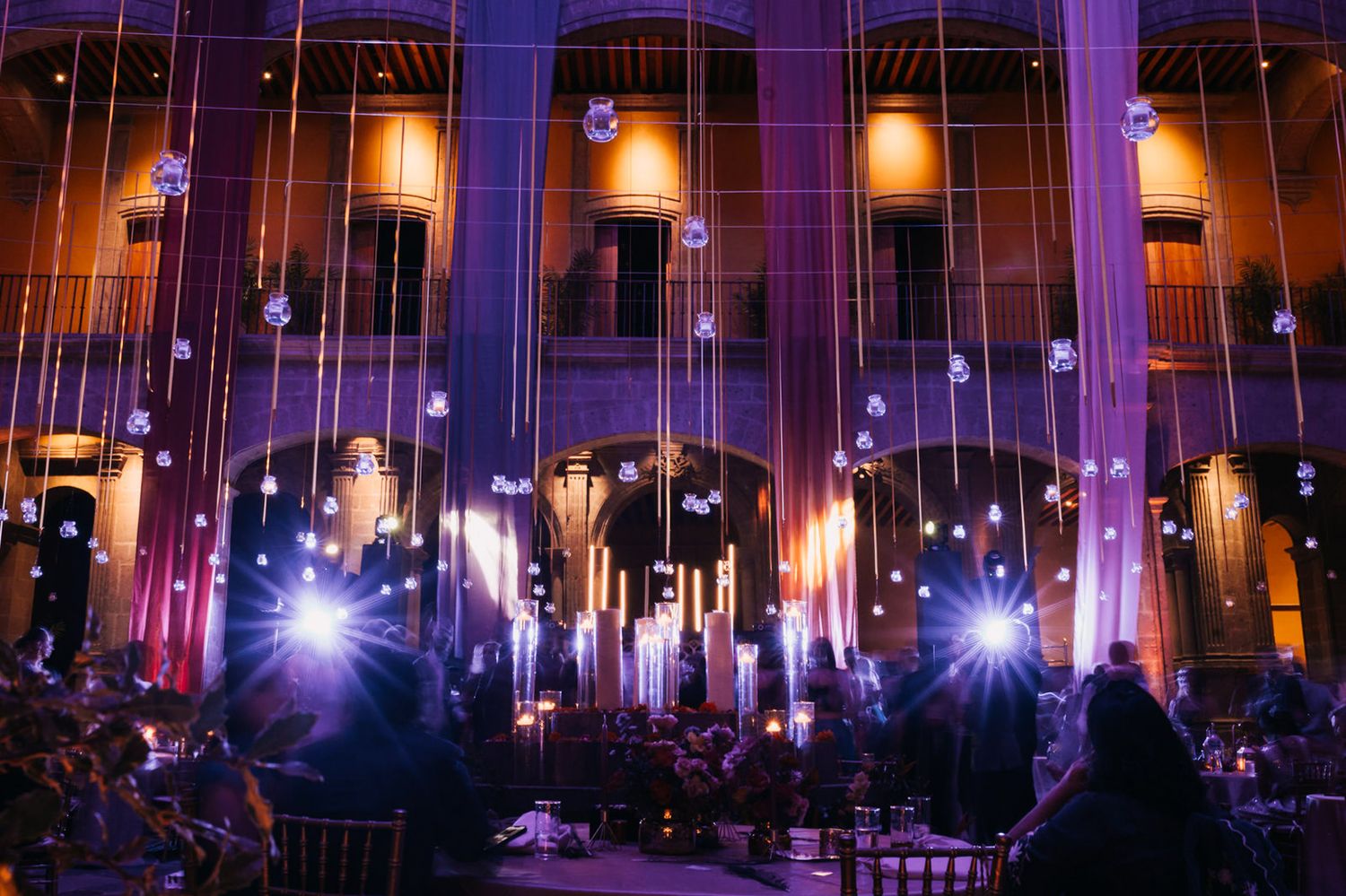 Stunning purple and gold lighting illuminates hanging crystal decorations at a grand wedding venue.
