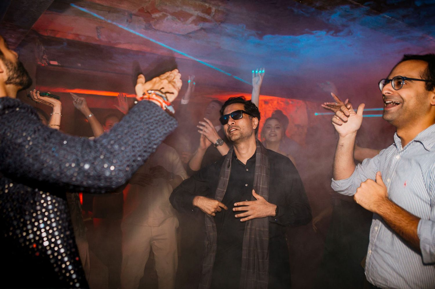 People dancing and celebrating at a vibrant nightclub party with colorful lights and fog effects.
