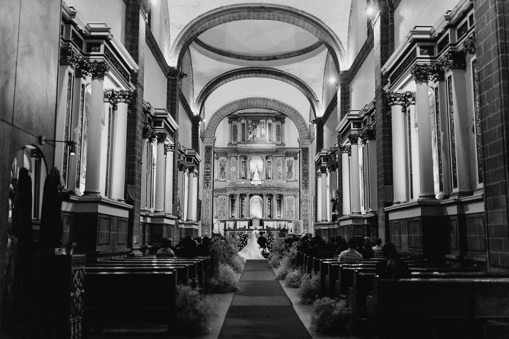 Black and white photo of a grand church interior with arched ceilings, ornate columns, and wedding ceremony at the altar.
