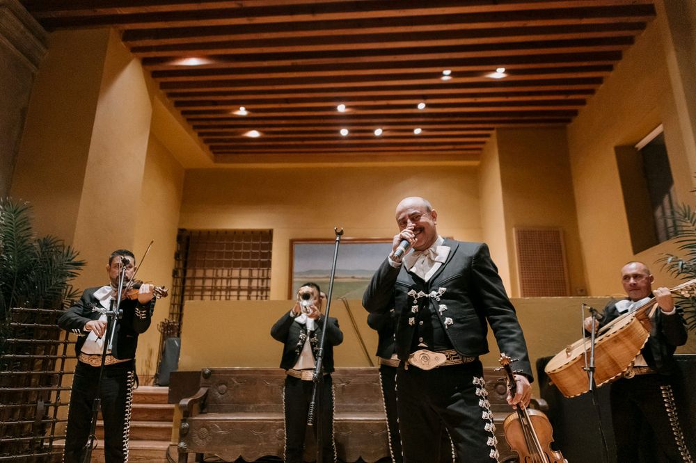 Mariachi band performs live music in a warmly lit venue with wooden ceiling beams.