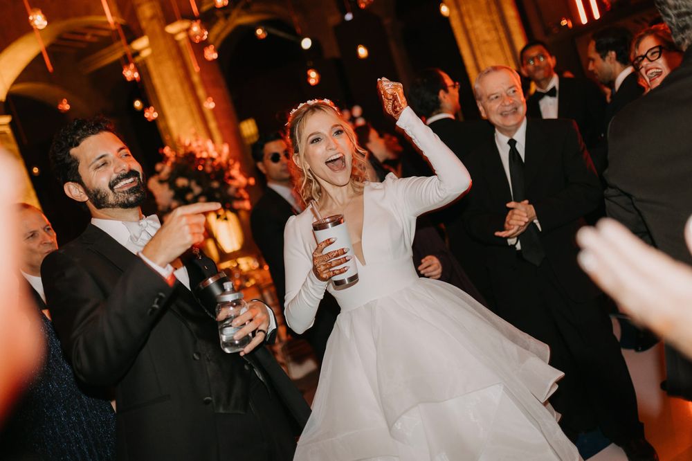 Joyful bride in white gown celebrating with guests on wedding dance floor.