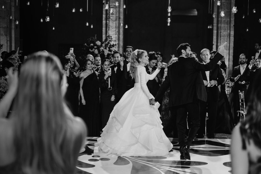 Black and white photo of bride and groom sharing first dance surrounded by guests at elegant wedding reception.