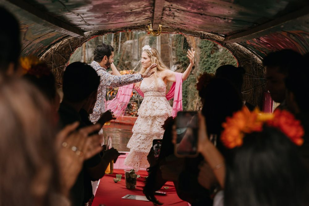 Bride in white lace dress celebrated under floral canopy with guests clapping at boho outdoor wedding.