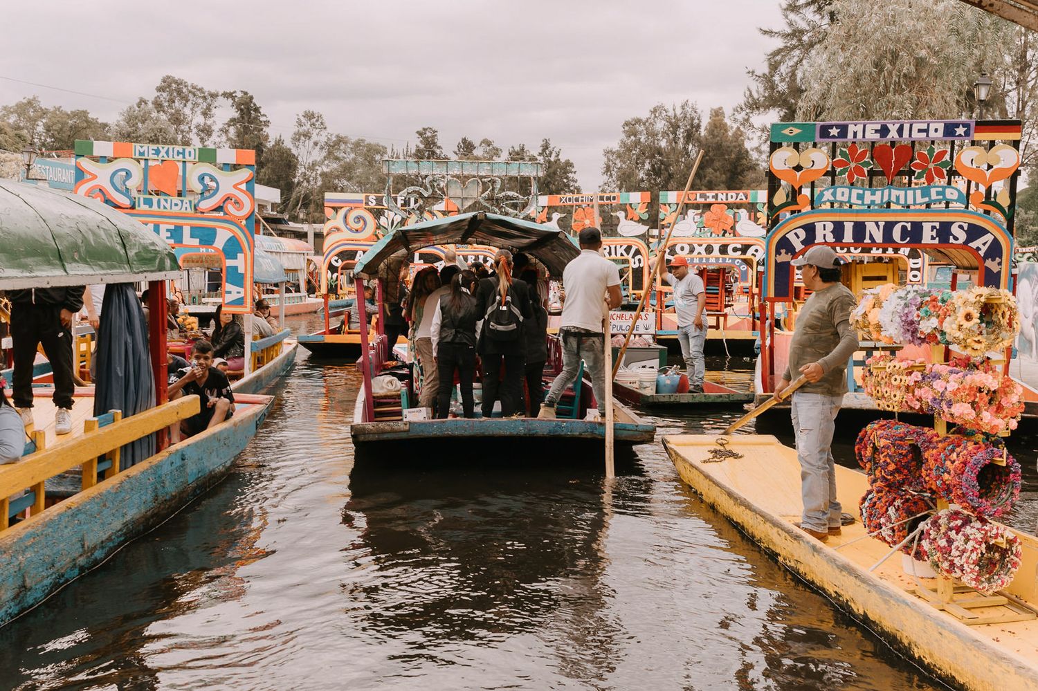 Colorful trajineras boats navigate the canals of Xochimilco, Mexico City, with vendors and tourists aboard.