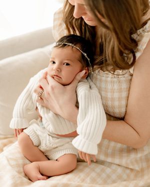 newborn baby girl and mom in photo on cream background and chair during photoshoot in Marion Indiana