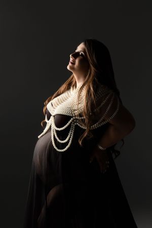 Moody maternity portrait with pearl accessories and dramatic lighting.