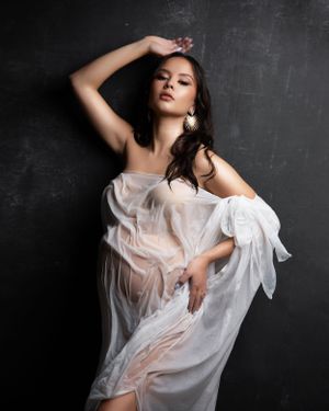 Artistic portrait with flowing white fabric against dark background creates ethereal mood.