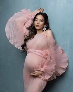 Dramatic maternity portrait in pleated pink dress with ruffled sleeves.