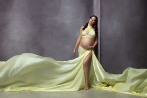 Elegant maternity portrait featuring flowing yellow gown against grey backdrop.
