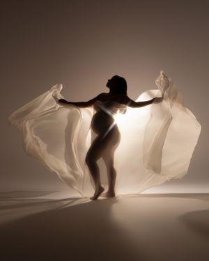 Artistic silhouette with flowing white fabric creating dramatic wing-like effect in backlit studio shot.