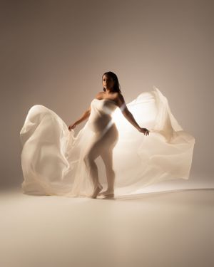 Graceful maternity portrait with billowing white fabric creating ethereal movement effect.