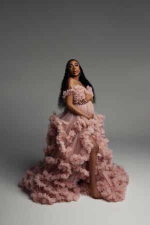 Stunning pink tulle ball gown with ruffled details and high slit in dramatic studio portrait.