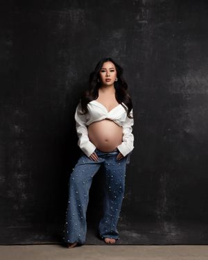 Casual maternity portrait in white cropped top and pearl-studded jeans.