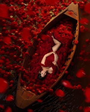Artistic portrait in wooden boat surrounded by red rose petals.