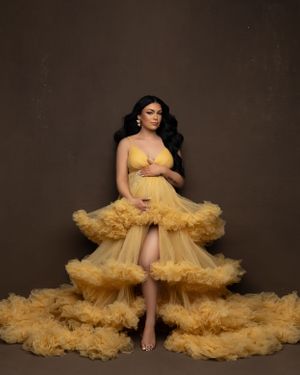 Figure wearing layered yellow tulle gown poses against dark background.