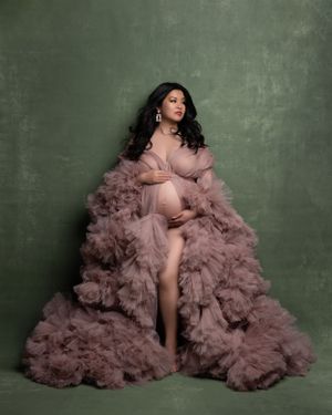 Elegant maternity portrait with voluminous mauve tulle gown against green backdrop.