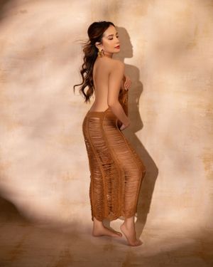 Artistic portrait in a fitted brown dress against a warm neutral background.