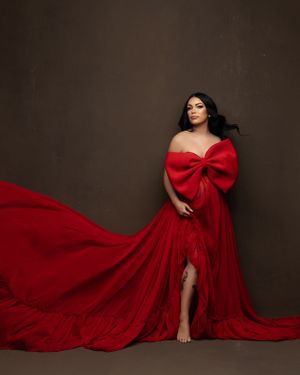 Dramatic red gown with oversized bow flows gracefully against dark background.