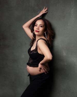 Dramatic maternity portrait in black lace against a dark grey textured wall.