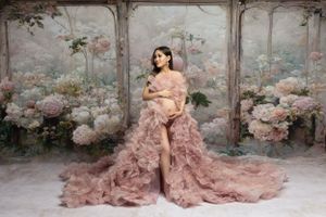 Romantic maternity portrait in blush tulle gown surrounded by pink roses in garden setting.
