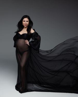 Dramatic maternity photo with flowing black sheer gown against grey background.