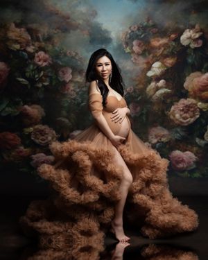 Artistic maternity portrait with peach tulle dress against floral backdrop.