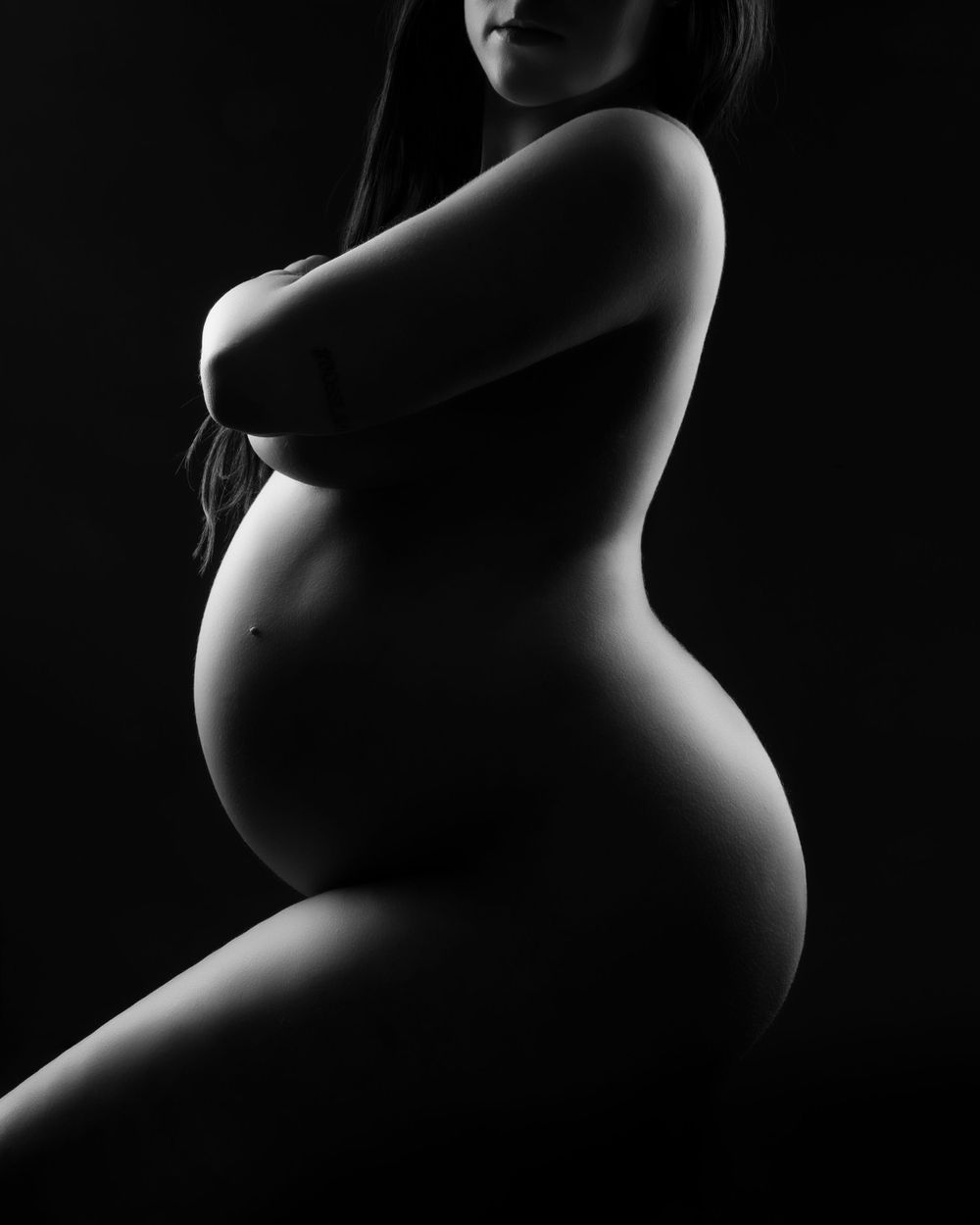Artistic black and white silhouette photograph capturing the curves of a pregnant woman's form in dramatic lighting.