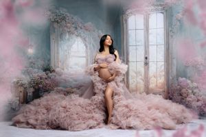 Dreamy maternity portrait in pink ruffled gown surrounded by cherry blossoms and french doors.