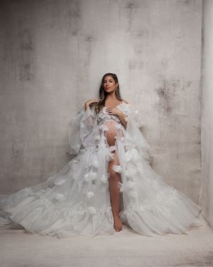 Ethereal maternity portrait in flowing white ruffled gown against textured gray background.