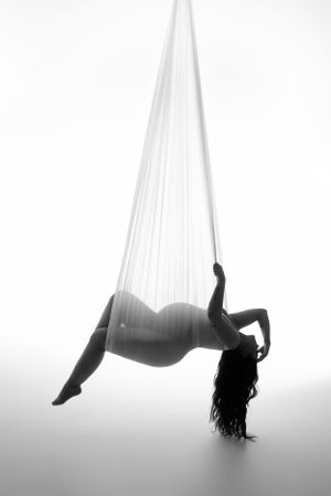 Artistic black and white silhouette of aerial performer suspended in silk fabric.