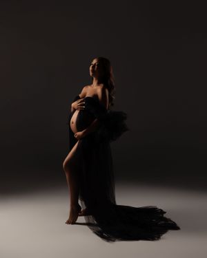 Dramatic silhouette of expectant mother in black flowing fabric against dark studio background.