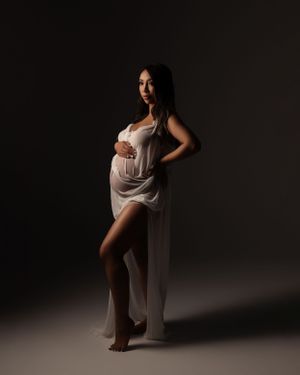 Artistic maternity portrait in white draped fabric showing elegant pose against dark backdrop.