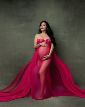 Dramatic maternity portrait in flowing fuchsia gown against dark grey backdrop.