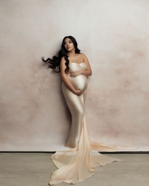 Elegant maternity portrait in form-fitting champagne silk gown with train.