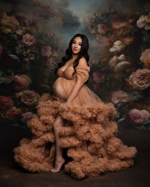 Artistic maternity portrait with peach tulle dress against floral backdrop.
