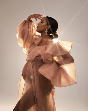 Artistic maternity portrait in warm peach-toned ruffled dress with sunlit glow.