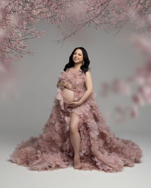 Maternity photo setup with cherry blossoms and dusty rose tulle gown against grey backdrop.