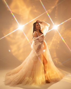 Glamorous maternity portrait in cream gown with dramatic light bursts and rainbow effects.